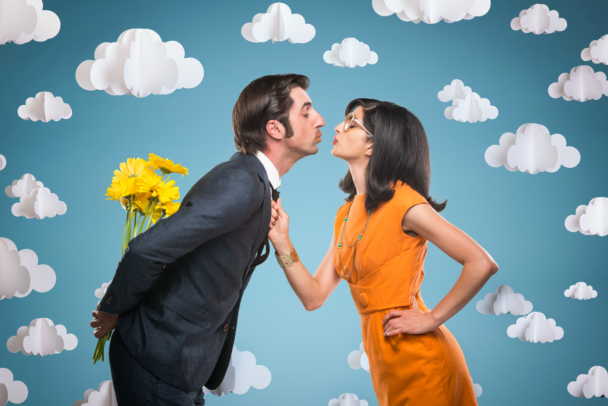 Quirky stylish couple with yellow Daisies about to kiss. The blue background has hanging 3-D paper clouds.